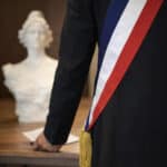 Vue de dos d’un élu local portant une écharpe tricolore, symbole du mandat municipal.