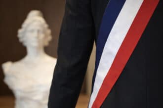 Vue de dos d’un élu local portant une écharpe tricolore, symbole du mandat municipal.