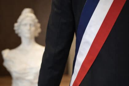 Vue de dos d’un élu local portant une écharpe tricolore, symbole du mandat municipal.