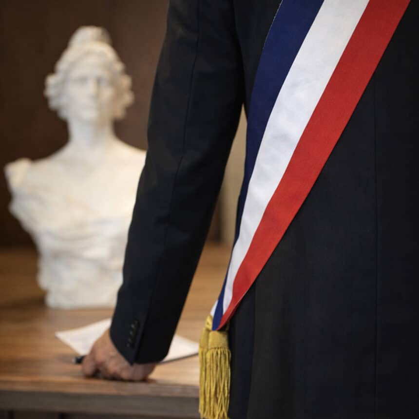 Vue de dos d’un élu local portant une écharpe tricolore, symbole du mandat municipal.